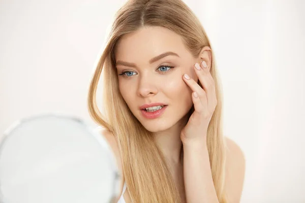 Maquillaje y belleza. Mujer tocando la piel de la cara mirando en espejo — Foto de Stock