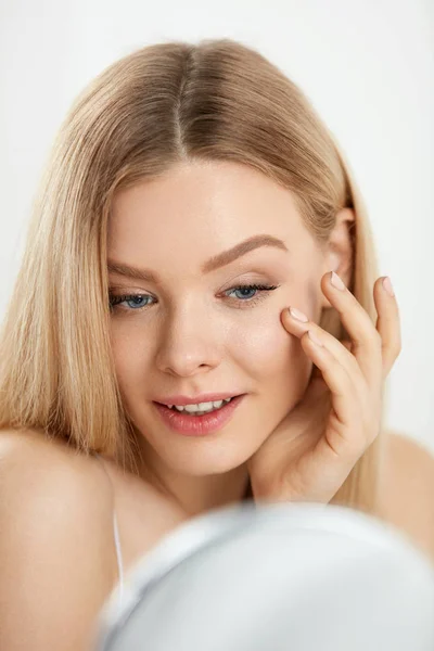 Maquillaje y belleza. Mujer tocando la piel de la cara mirando en espejo — Foto de Stock