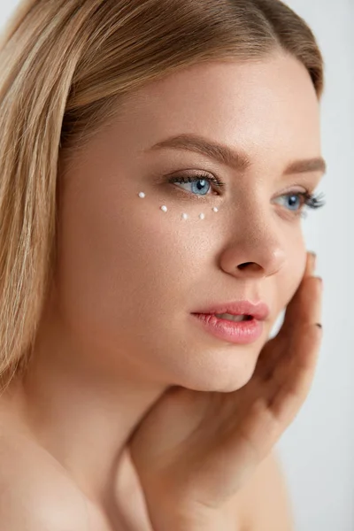 Cuidados faciais. Mulher com gotas de creme cosmético sob o olho — Fotografia de Stock