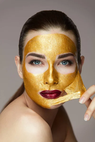 Frau Gesicht Schönheit. Mädchen steigt aus kosmetischer Goldmaske von der Haut — Stockfoto