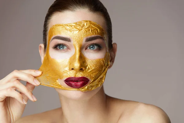 Perempuan Wajah Kecantikan. Girl getting off Cosmetic Gold Mask From Skin — Stok Foto