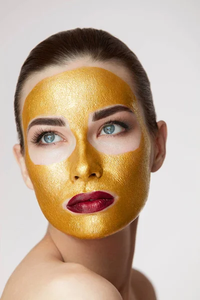 Cosméticos de belleza. Mujer joven con máscara de oro en la piel suave —  Fotos de Stock