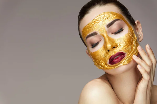 Cosmetisch Product. Mooi meisje met gouden masker gezicht aan te raken — Stockfoto