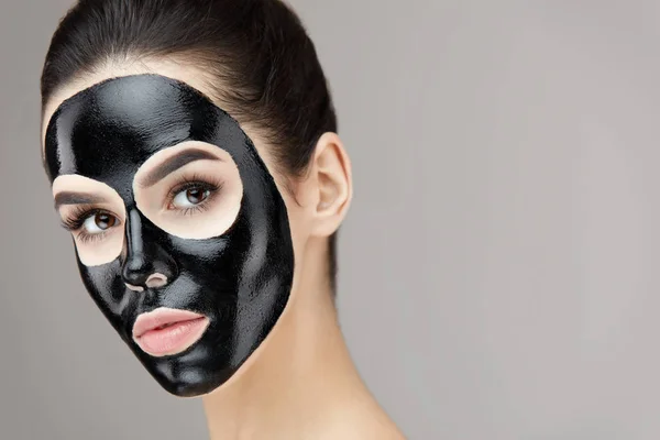 Красивая женщина лицо с косметической черной пилинг маска на коже — стоковое фото
