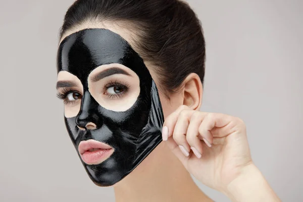 Περιποίηση προσώπου γυναίκα. Όμορφη νεαρή γυναίκα αφαίρεση μαύρη μάσκα — Φωτογραφία Αρχείου