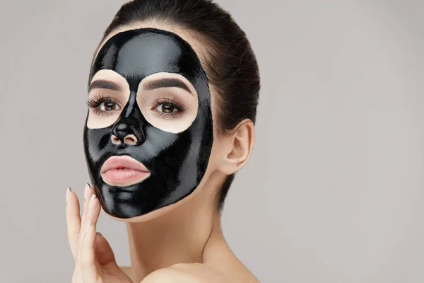 Kvindelig skønhed ansigt hud behandling. Pige med sort skræl maske - Stock-foto