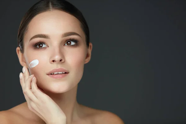 Cura della pelle di bellezza. Giovane donna con trucco naturale che applica la crema — Foto Stock