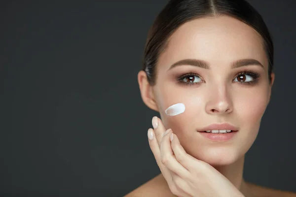 Cura della pelle di bellezza. Giovane donna con trucco naturale che applica la crema — Foto Stock