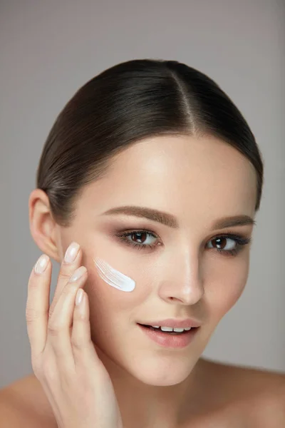 Cosméticos de belleza. Mujer poniendo crema cosmética en cara hermosa — Foto de Stock