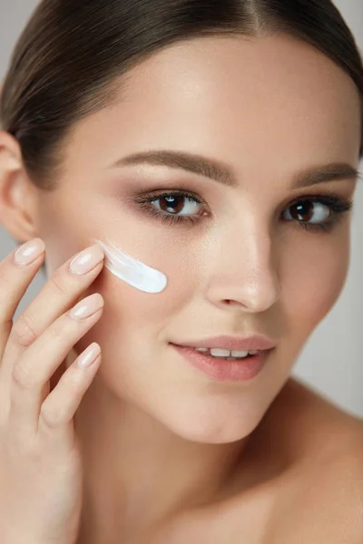 Cosméticos de belleza. Mujer poniendo crema cosmética en cara hermosa —  Fotos de Stock