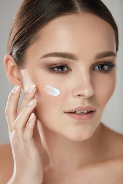 Cosméticos de belleza. Mujer poniendo crema cosmética en cara hermosa —  Fotos de Stock