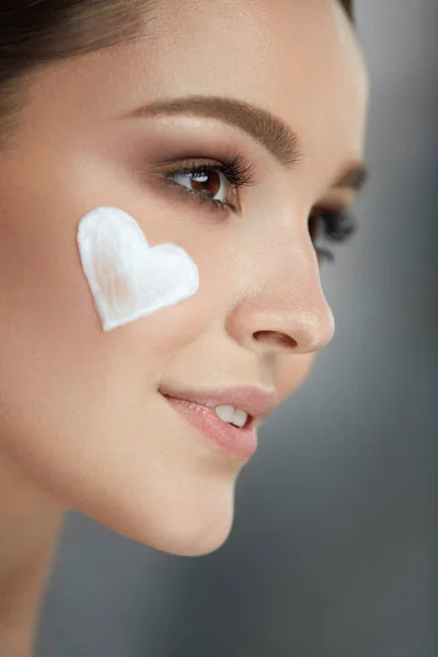 Cuidado de la piel de belleza. Mujer con corazón de crema en la cara — Foto de Stock