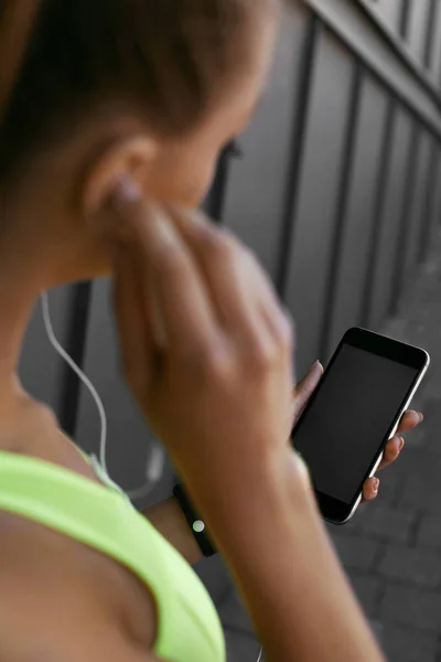 Kvinna lyssnar musik på telefon medan du tränar utomhus — Stockfoto