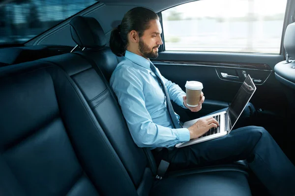 Homme travaillant sur ordinateur portable et boire du café dans la voiture . — Photo
