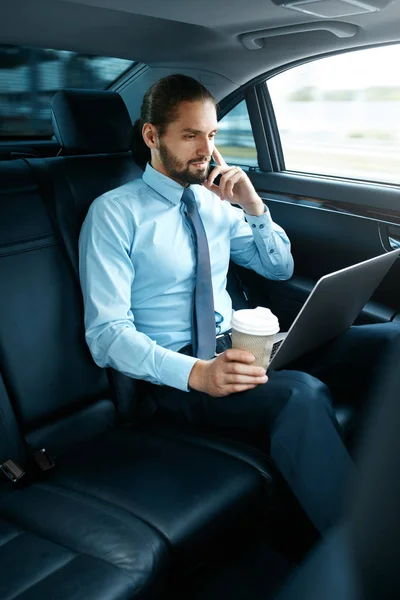 Человек работает над ноутбуком и пьет кофе в машине . — стоковое фото