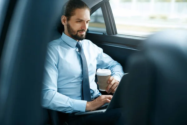Muž pracuje na notebooku a pití kávy v autě. — Stock fotografie