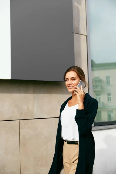 通りを歩きながら携帯電話で話している専門職の女性. — ストック写真