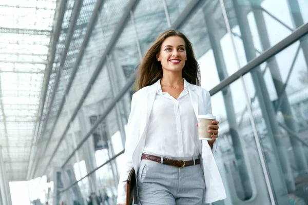 Hermosa mujer caminando con taza de café cerca del edificio de oficinas . —  Fotos de Stock