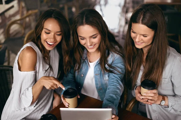 Друзі в кафе. Красиві усміхнені дівчата використовують планшет . — стокове фото