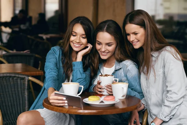 Jóvenes amigas usando teléfono y tomando café en el café . — Foto de Stock