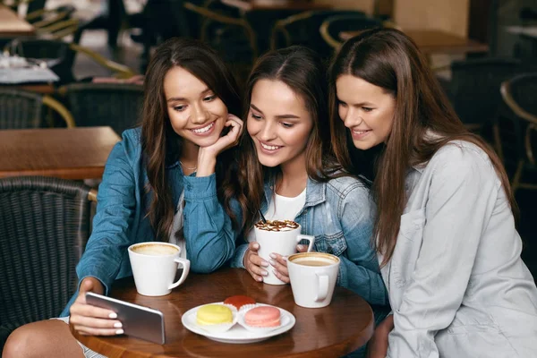 Jeunes amies utilisant le téléphone et boire du café dans le café . — Photo