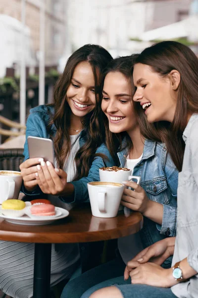 Jóvenes amigas usando teléfono y tomando café en el café . — Foto de Stock