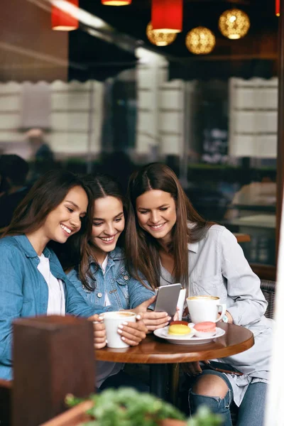 Jóvenes amigas usando teléfono y tomando café en el café . — Foto de Stock