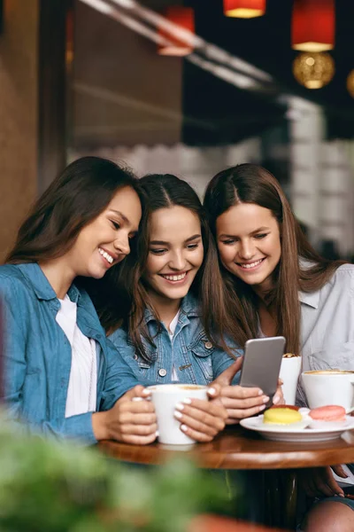 Jóvenes amigas usando teléfono y tomando café en el café . — Foto de Stock