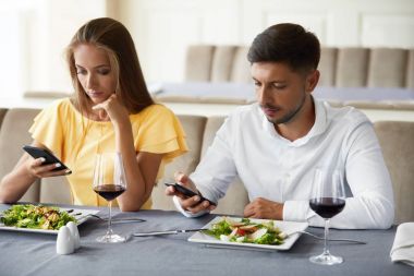 Telefonunu restoranda akşam yemeği kullanarak çift.