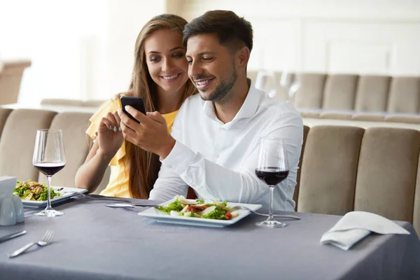 Couple amoureux regardant au téléphone ayant dîner au restaurant . — Photo