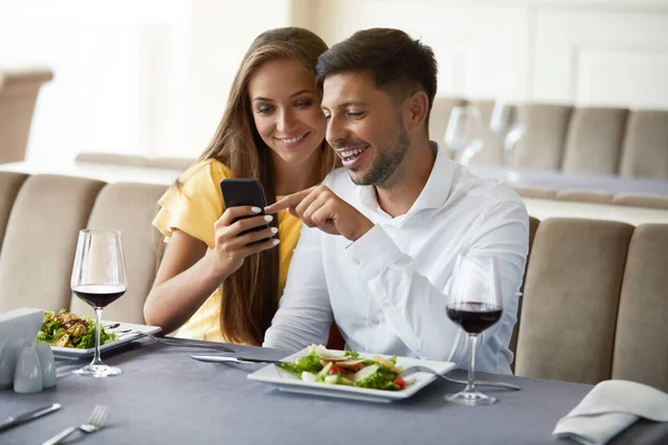 Couple amoureux regardant au téléphone ayant dîner au restaurant . — Photo