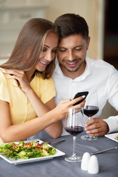 Couple amoureux regardant au téléphone ayant dîner au restaurant . — Photo