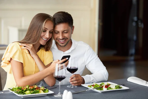 Casal apaixonado olhando no telefone jantando no restaurante . — Fotografia de Stock