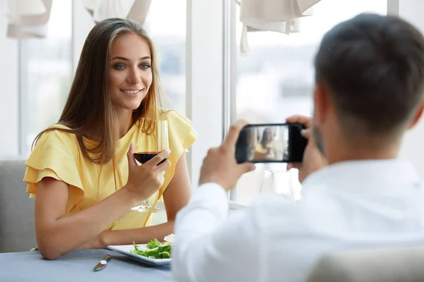 Casal no restaurante. Homem fazendo foto da mulher no telefone — Fotografia de Stock