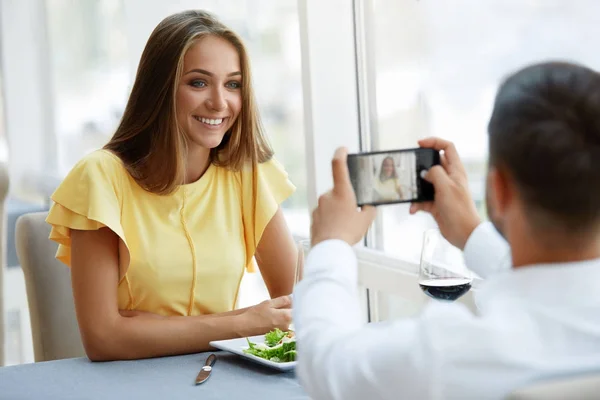 Casal no restaurante. Homem fazendo foto da mulher no telefone — Fotografia de Stock