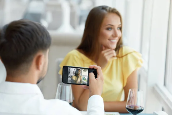 夫妇在餐厅。男人在电话里拍女人的照片 — 图库照片