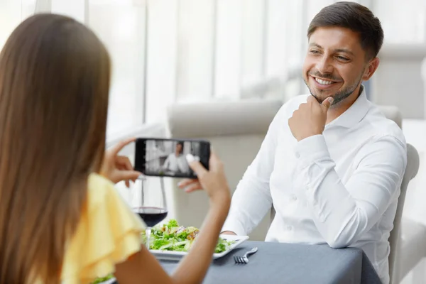 Jantar romântico. Mulher tirando fotos de homem no restaurante — Fotografia de Stock