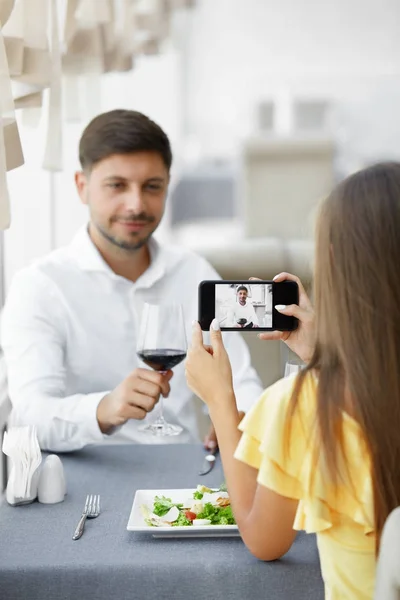 Jantar romântico. Mulher tirando fotos de homem no restaurante — Fotografia de Stock