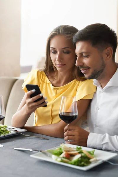 Casal apaixonado olhando no telefone jantando no restaurante . — Fotografia de Stock