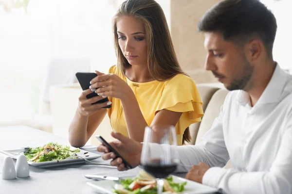 Pár pomocí telefonů na večeři v restauraci. — Stock fotografie