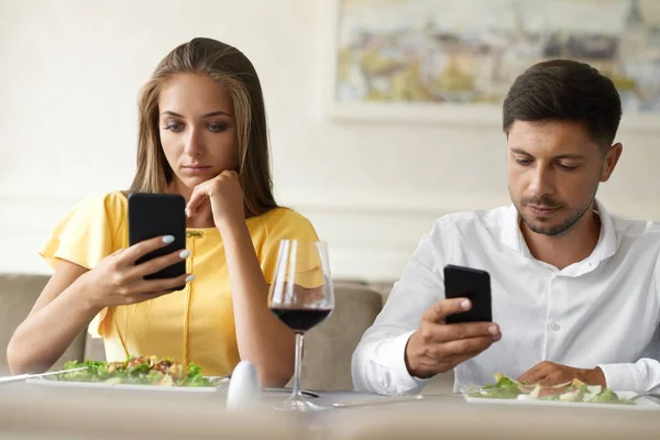 Couple Using Phones On Dinner In Restaurant.