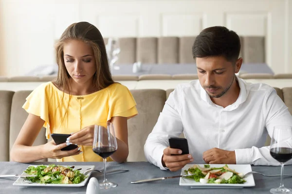 Пара с помощью телефонов на ужин в ресторане . — стоковое фото