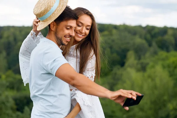 Romántico. feliz pareja en amor tomando fotos en teléfono en la naturaleza — Foto de Stock