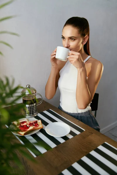 Mujer bebiendo café y desayunando por la mañana en la cocina — Foto de Stock