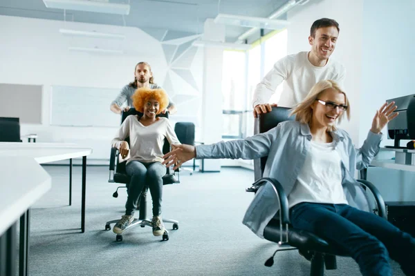 Büro. Menschen, die Spaß haben und auf Stühlen rasen. — Stockfoto
