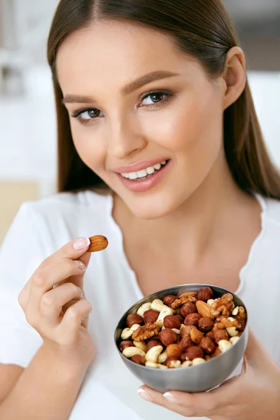 Sorrindo mulher comendo nozes na cozinha — Fotografia de Stock