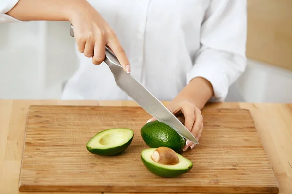 Dieta. Mãos femininas cortando abacate na cozinha . — Fotografia de Stock