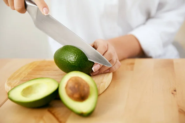 Dieta. Mãos femininas cortando abacate na cozinha . — Fotografia de Stock