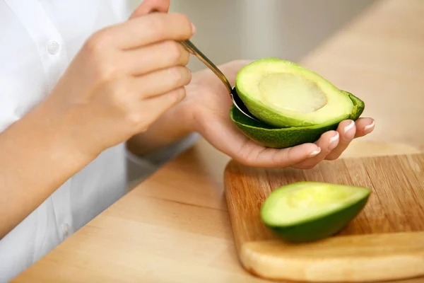 Avocado essen. Frauenhände schälen frische Avocado mit Löffel — Stockfoto