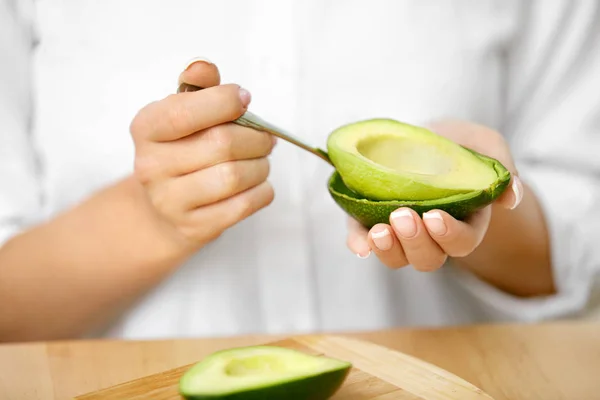 Avocado essen. Frauenhände schälen frische Avocado mit Löffel — Stockfoto